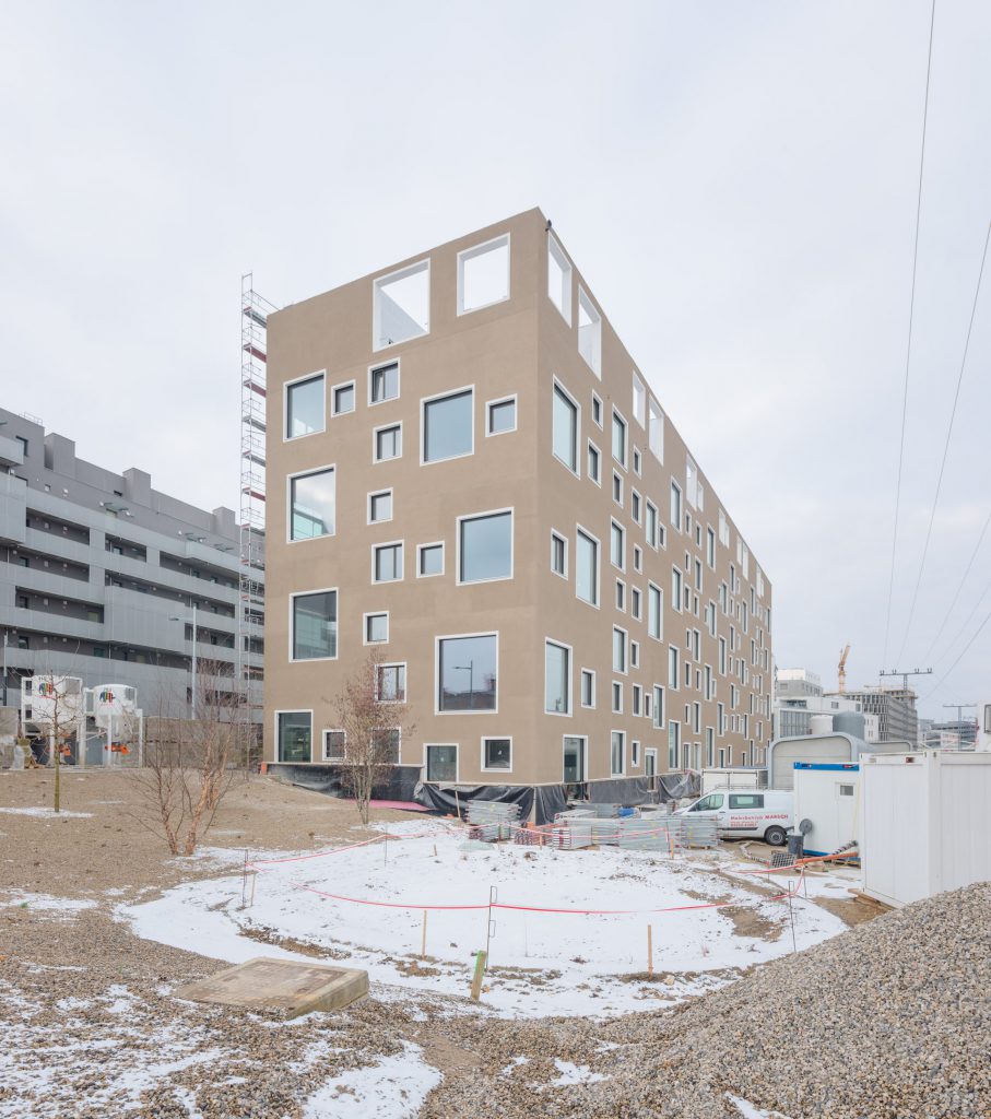 Neubaublock in hellbraun mit verschieden großen Fenstern