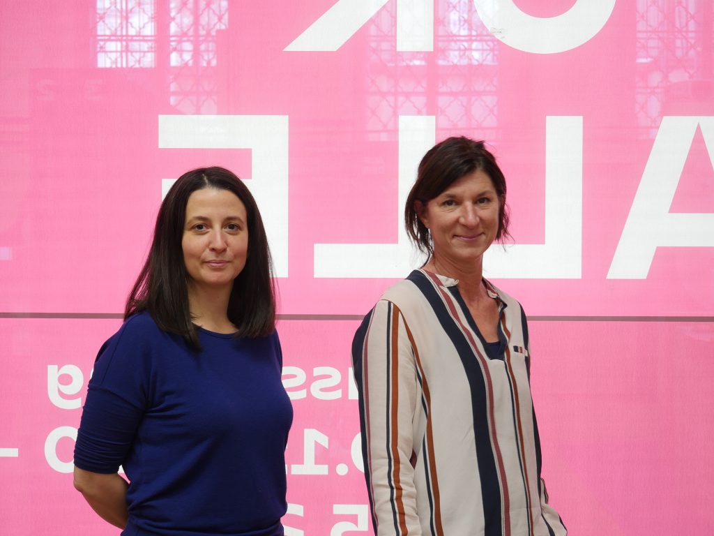 Two women against a pink background