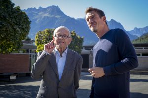 ein alter Mann mit Brille und ein junger Mann stehen im Sonnenschein vor einer Bergkulisse