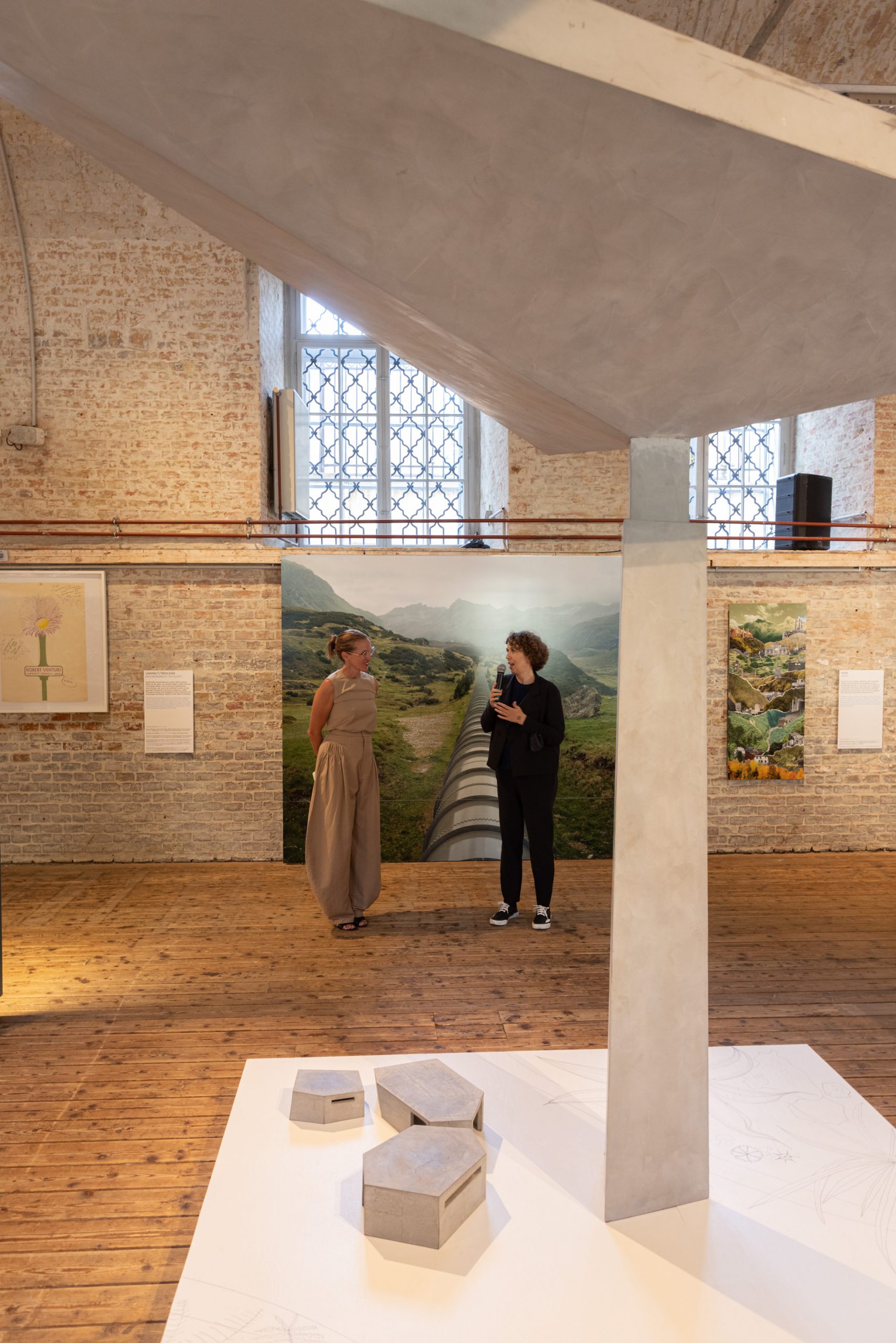 2 women in front of a large background photo and a concrete umbrella in front of it