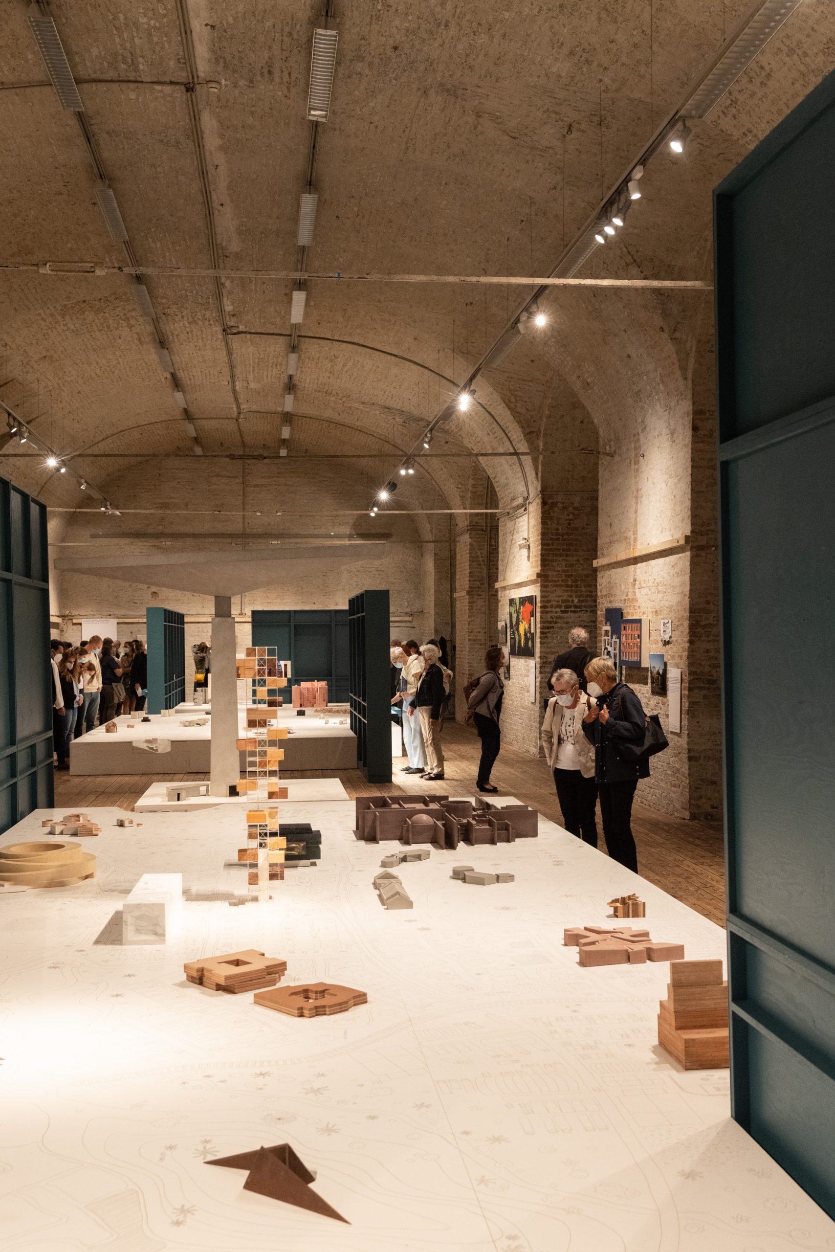 Ausstellungsraum mit Ziegeldecke, in der Mitte auf weißem Untergrund viele Modelle und hohen petrolfarbenen Regalen