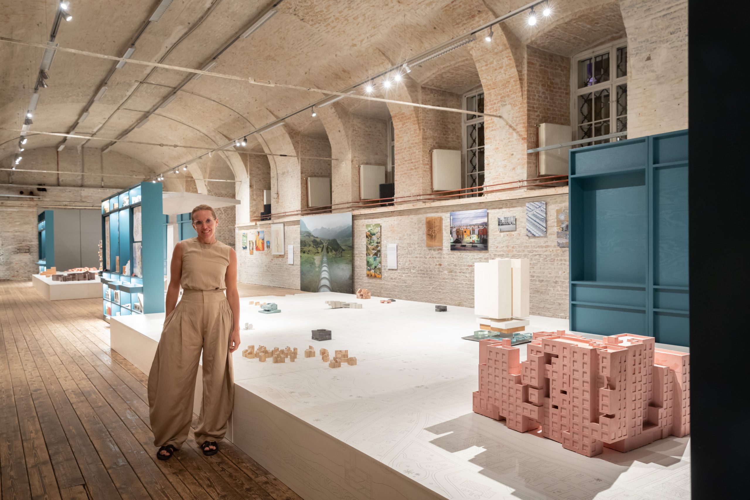 Woman in light brown trouser suit and glasses in front of exhibition objects