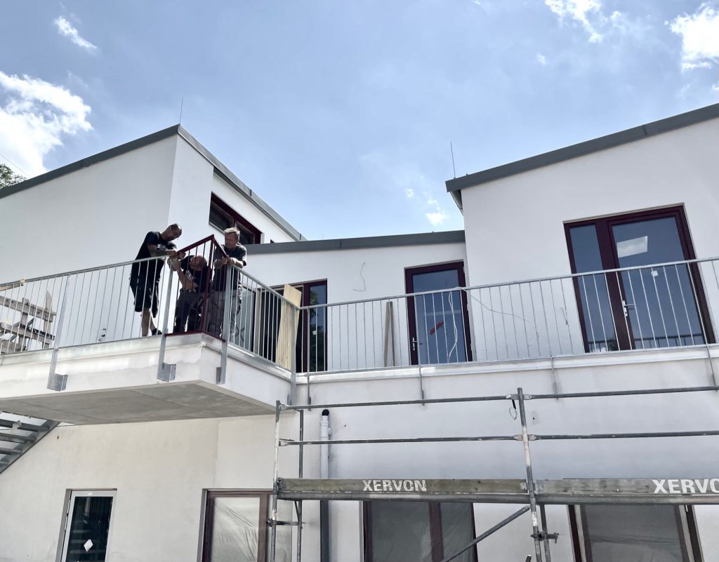 3 Männer arbeiten an einem Geländer bei einem Haus