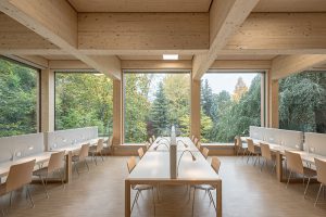 Long light wooden tables in large wooden room with large windows