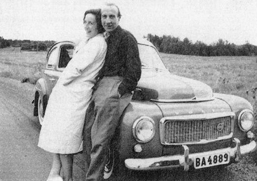 Black and white photo of a woman and a man leaning against a car