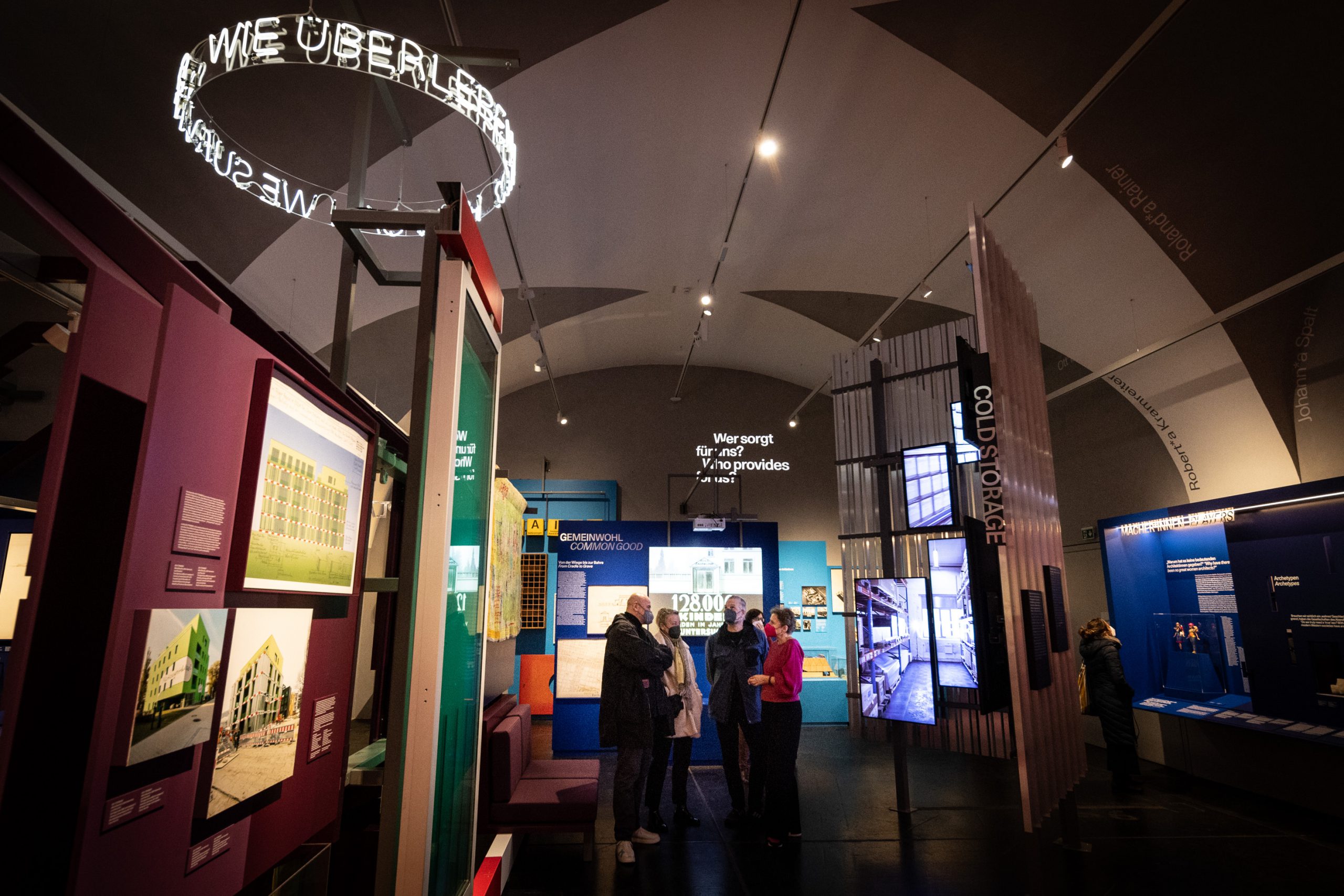 mehrere Personen in einem Ausstellungsraum mit vielen bunten Wänden, Tafeln, Screens