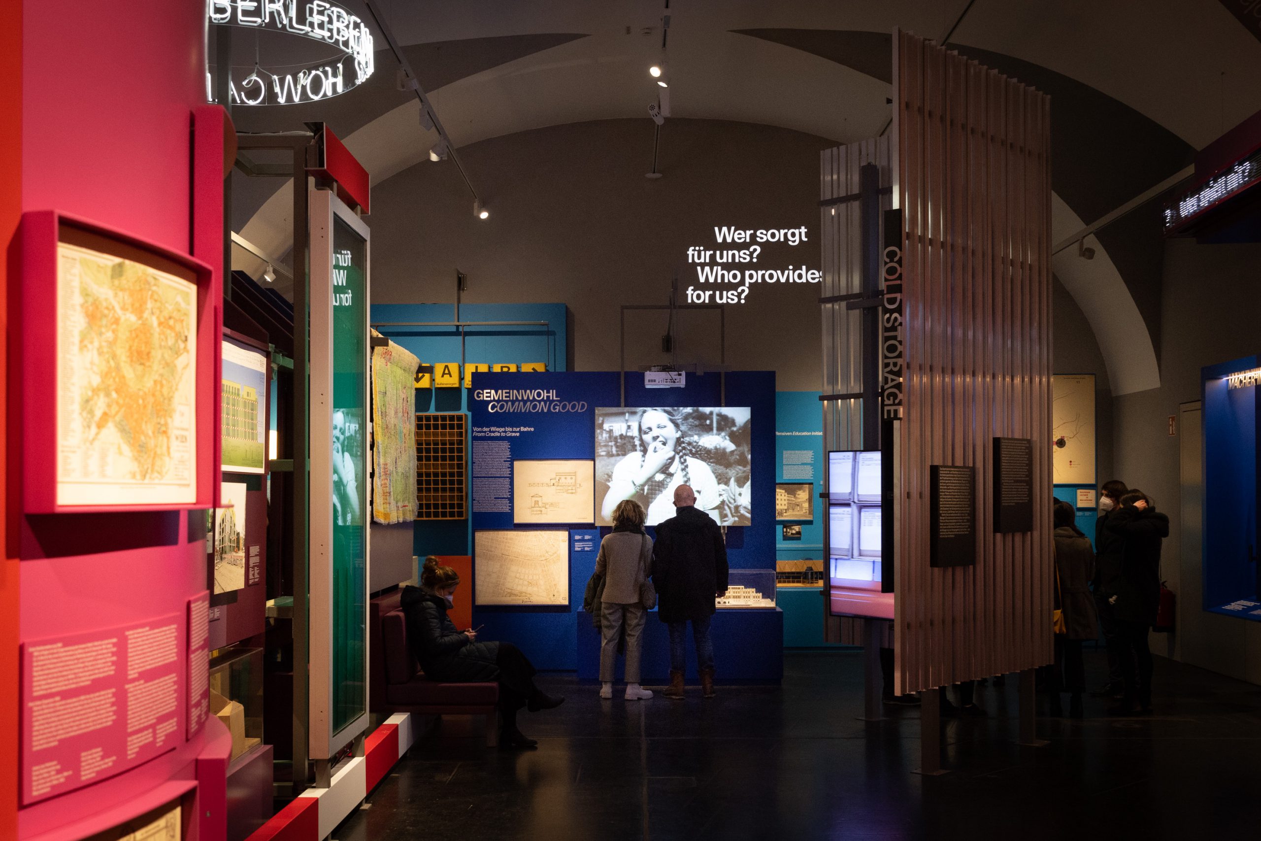 Ausstellungsraum mit bunten Installationen und 2 Personen vor einem Screen