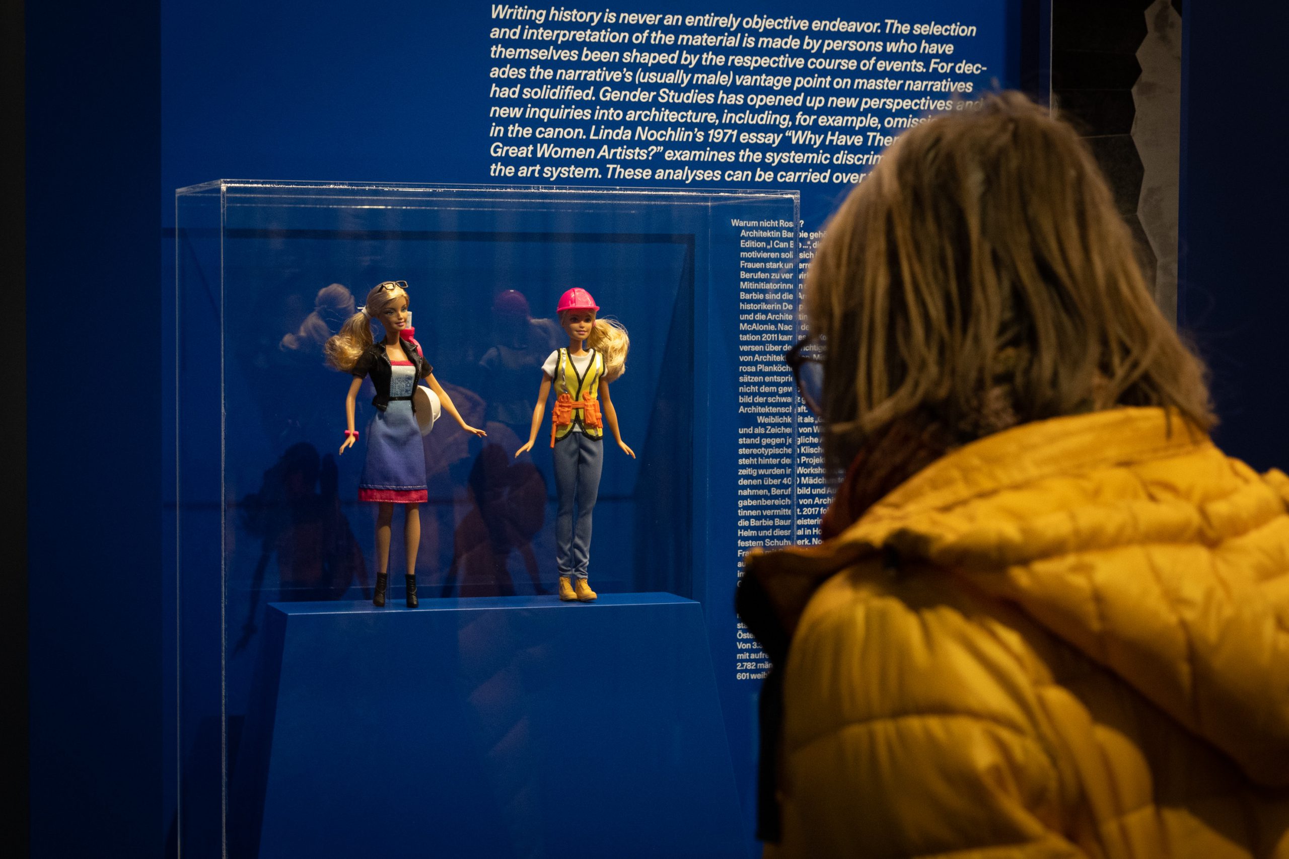 Frau steht vor blauer Vitrine mit 2 Barbiepuppen darin