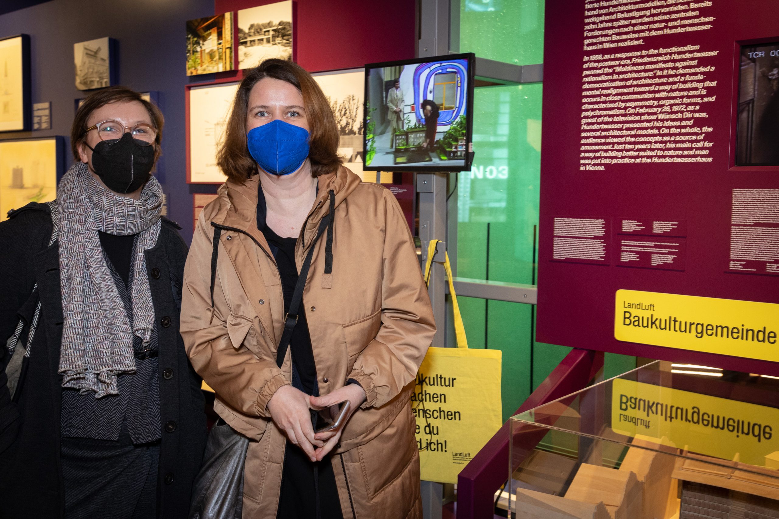 2 Frauen mit Maske vor Ausstellungswand mit gelben Schildern