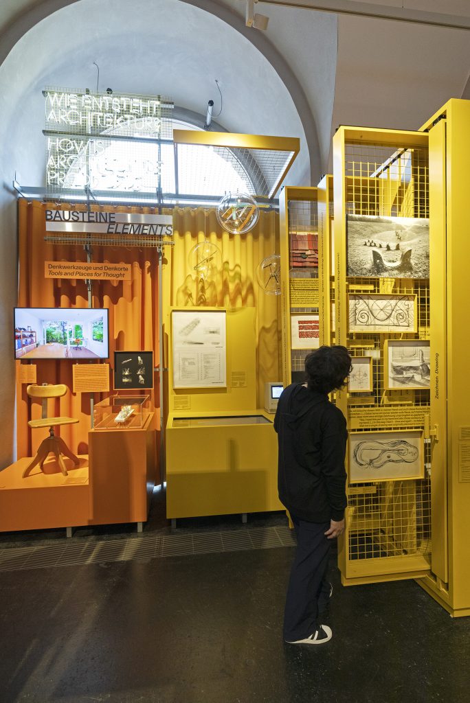 Person dressed in black in front of yellow-orange exhibition wall