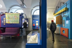 2 people looking at exhibition, blue walls, purple-coloured seating furniture