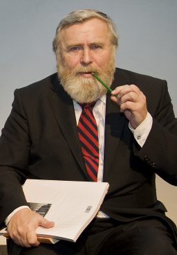 A man with a striped tie, holding a pad and a green pencil in his mouth
