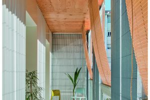 View of a sunlit corridor with green and turquoise armchairs and wooden ceiling and blinds