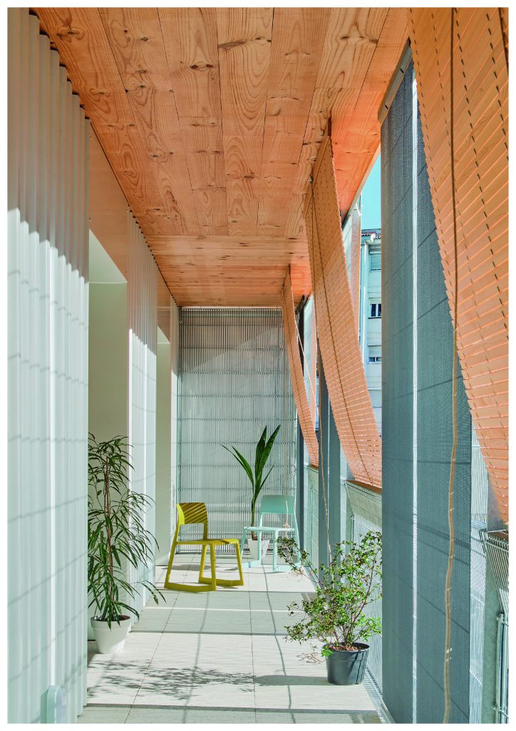 View of a sunlit corridor with green and turquoise armchairs and wooden ceiling and blinds