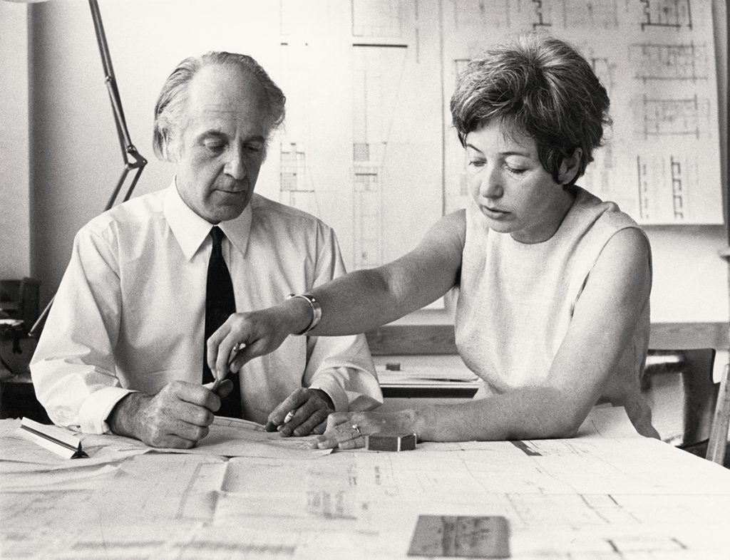 black and white photo of a man and a woman looking at a big plan