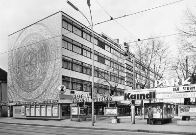 black and white photo with building and advertising signs in front of it