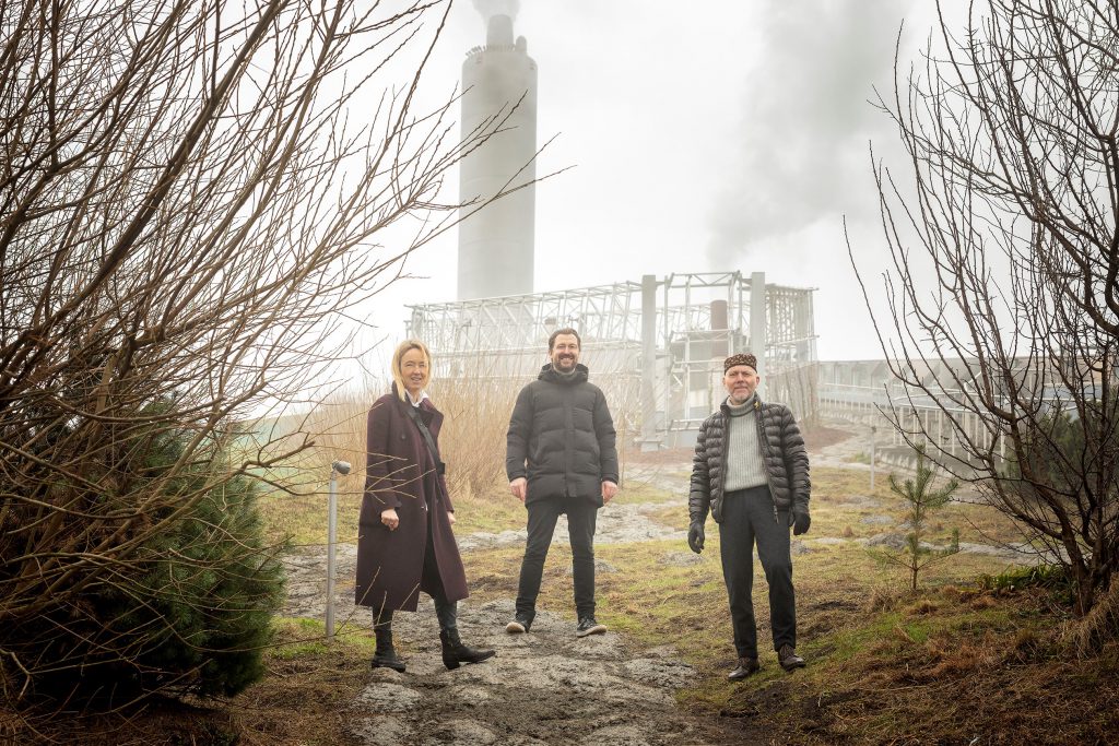 1 woman, 2 men in foggy landscape with factory in the background