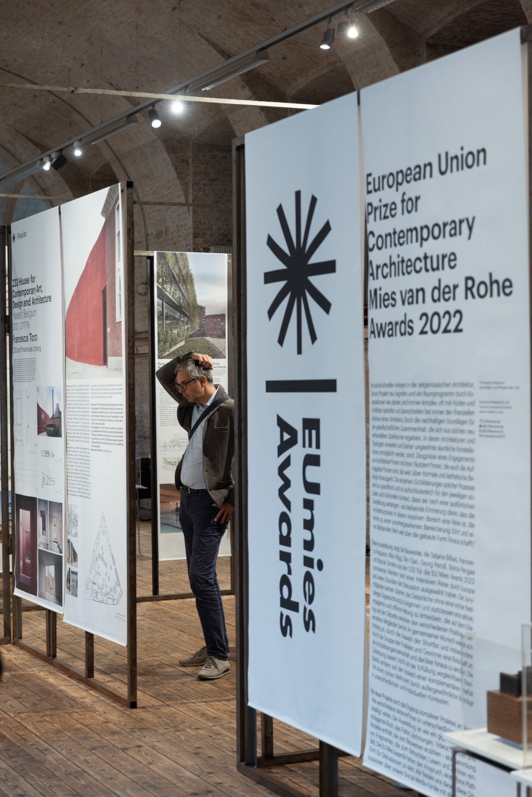 Exhibition with large tarpaulins on which a star with EUmies Awards, behind it a man grabbing his head