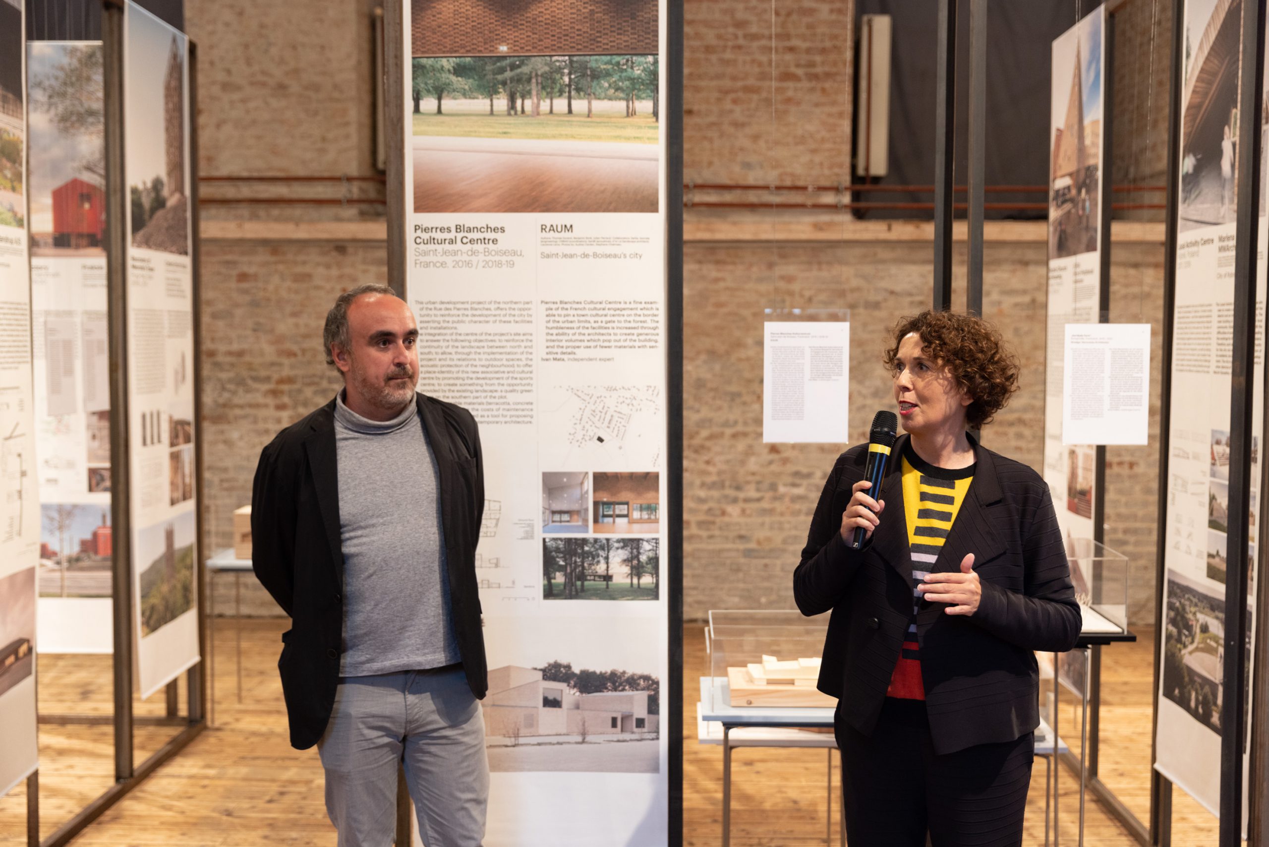 a man and a woman with a microphone in front of exhibition tarpaulins