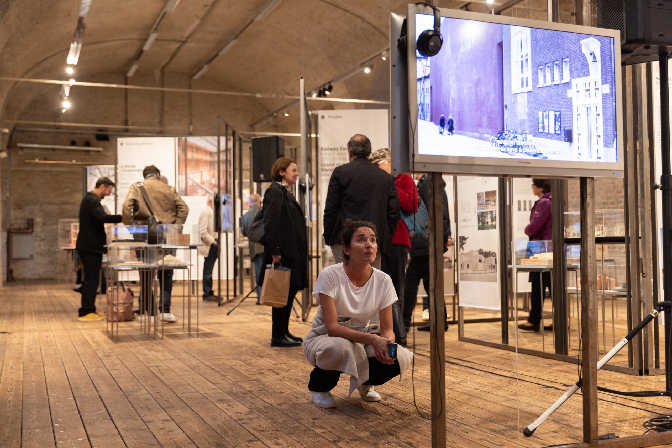 Kneeling woman in front of a screen, watching a film. Behind her, several people in an exhibition room