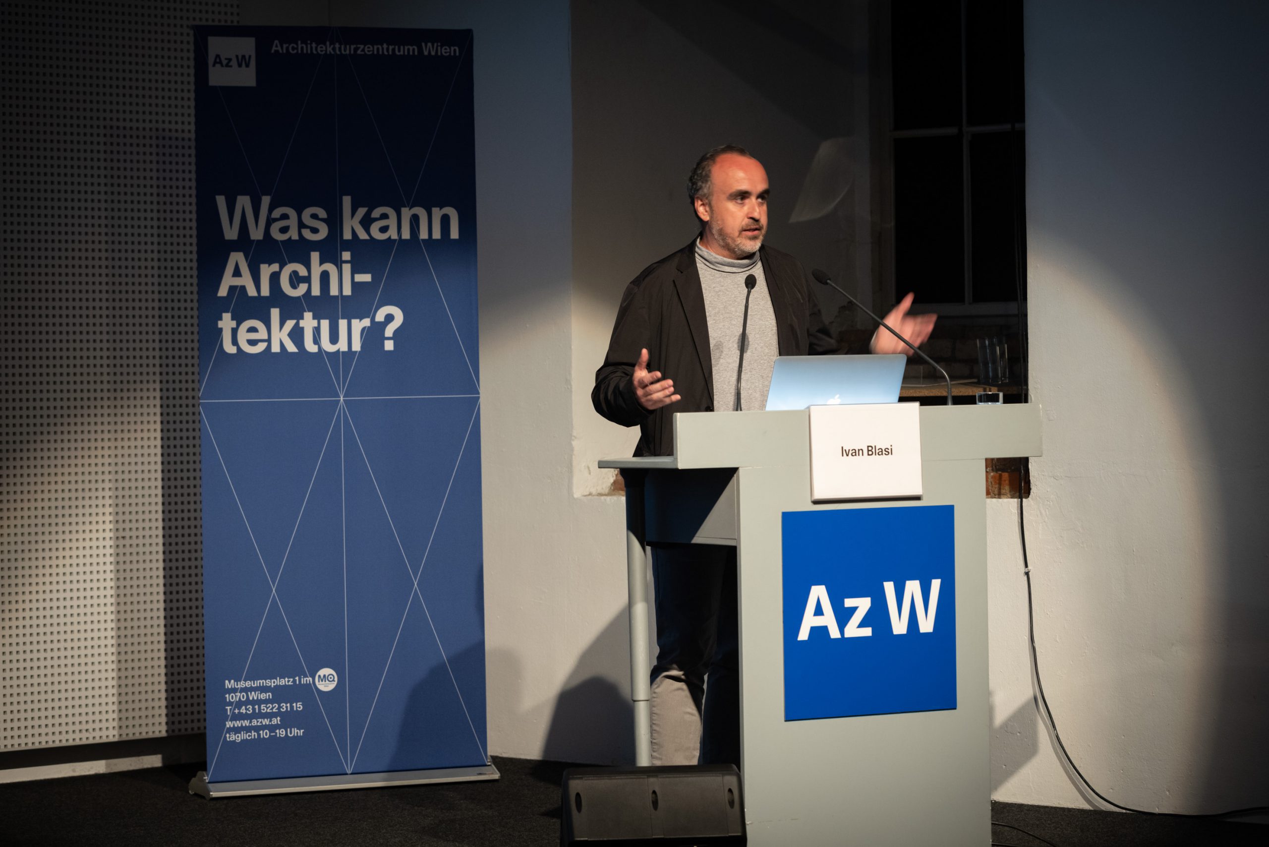Man standing behind a desk, in front of it a blue square with the lettering Az W
