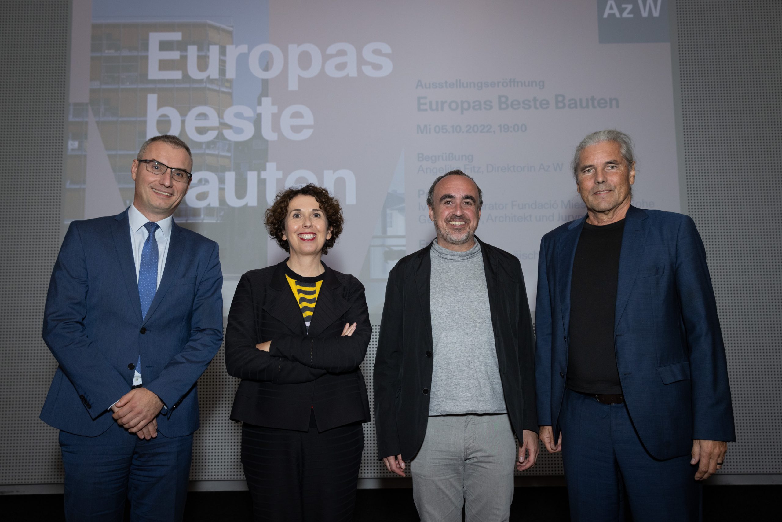4 people, one of them a woman, stand in front of a large screen with the words "Europe's best buildings"