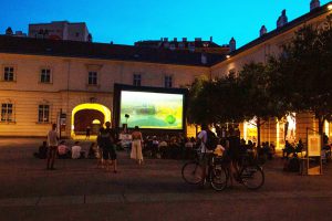 Canvas in a courtyard at dusk with people standing and sitting in front of it