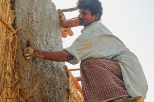 Man squatting on a high stool plastering a bamboo wall