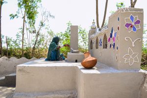 a veiled woman sits on a rise and stirs in a pot