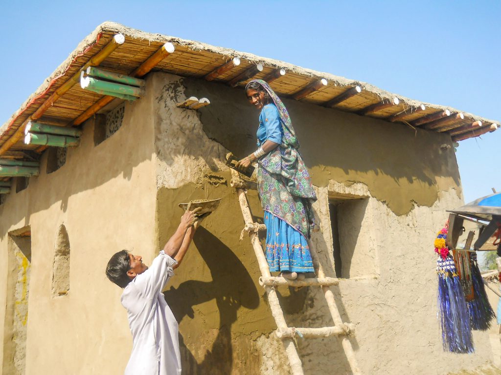 Woman with veil stands on a wooden ladder, a man hands her a bowl