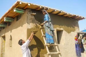 Woman with veil stands on a wooden ladder, a man hands her a bowl