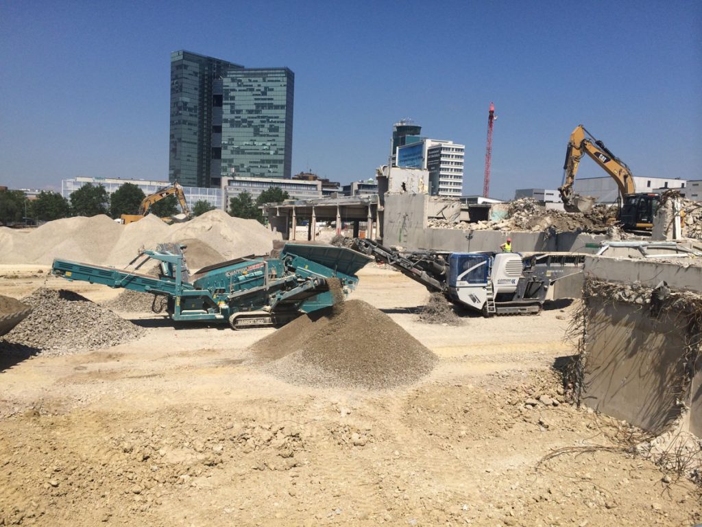 Construction site with several excavators and high-rise building in the background