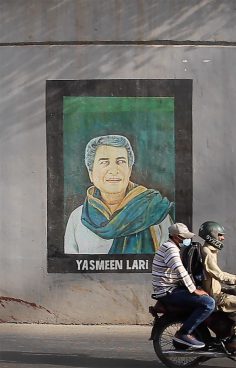 Mural of a woman with a green scarf, in front of it a moped with 2 riders on it