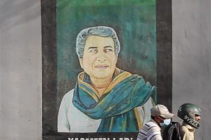Mural of a woman with a green scarf, in front of it a moped with 2 riders on it