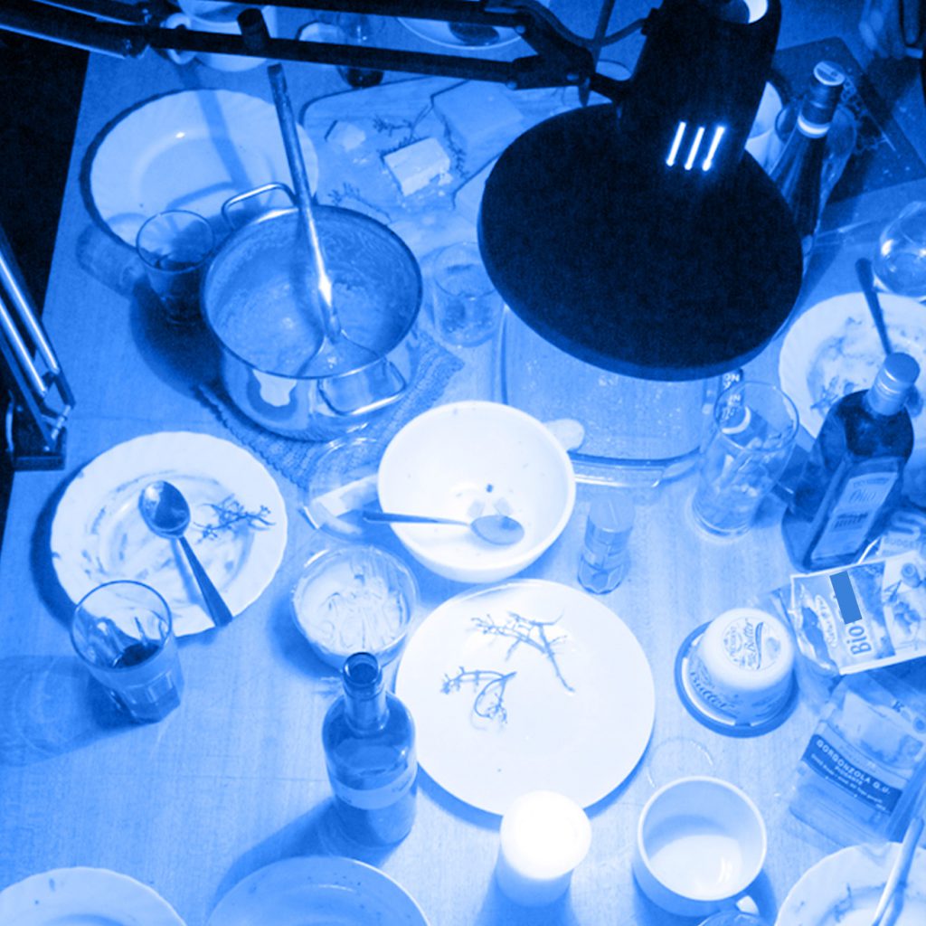 Photo in blue tone with a lot of dishes on a table and a desk lamp above it