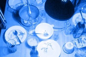 Photo in blue tone with a lot of dishes on a table and a desk lamp above it