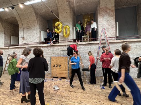 Several people in a brick hall, a ladder and a large wooden box with the inscription AZW standing in the room.