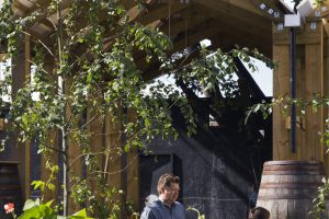 2 Menschen in einem Garten mit Hütte im Hintergrund, Bub hat Gartenschlauch in der Hand