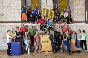Many colourfully dressed people in front of a brick wall, confetti flying through the air and the number 30 stuck to the wall
