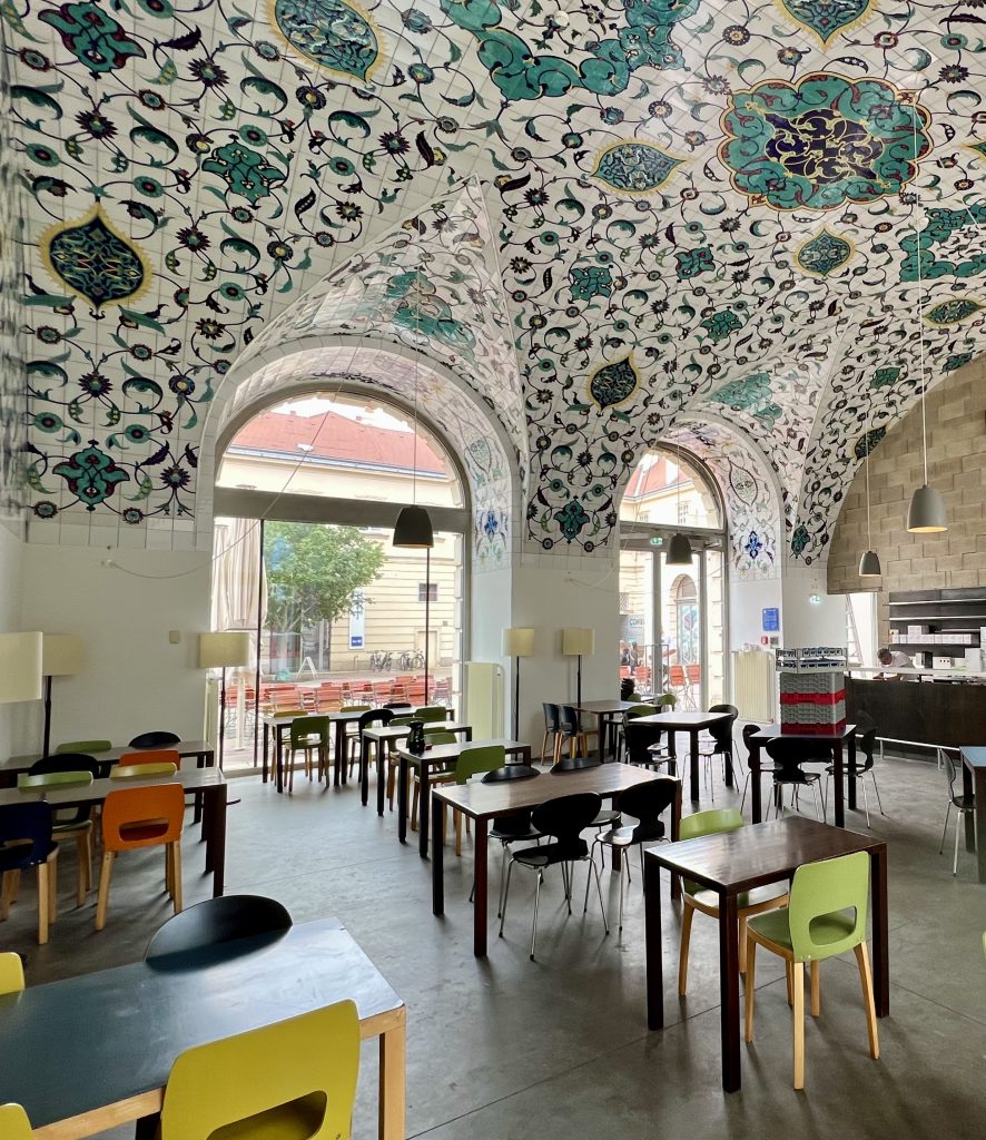 Cafe with many tables and armchairs and ornamental tile ceiling
