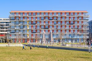rot farbenes Gebäude mit vielen Balkonen, davor großer Spielplatz mit Wiese