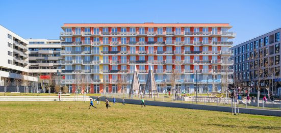 rot farbenes Gebäude mit vielen Balkonen, davor großer Spielplatz mit Wiese