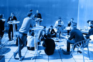 blue coloured photo with people sitting, standing and eating