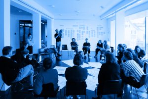 blue coloured photo with several people sitting in a circle