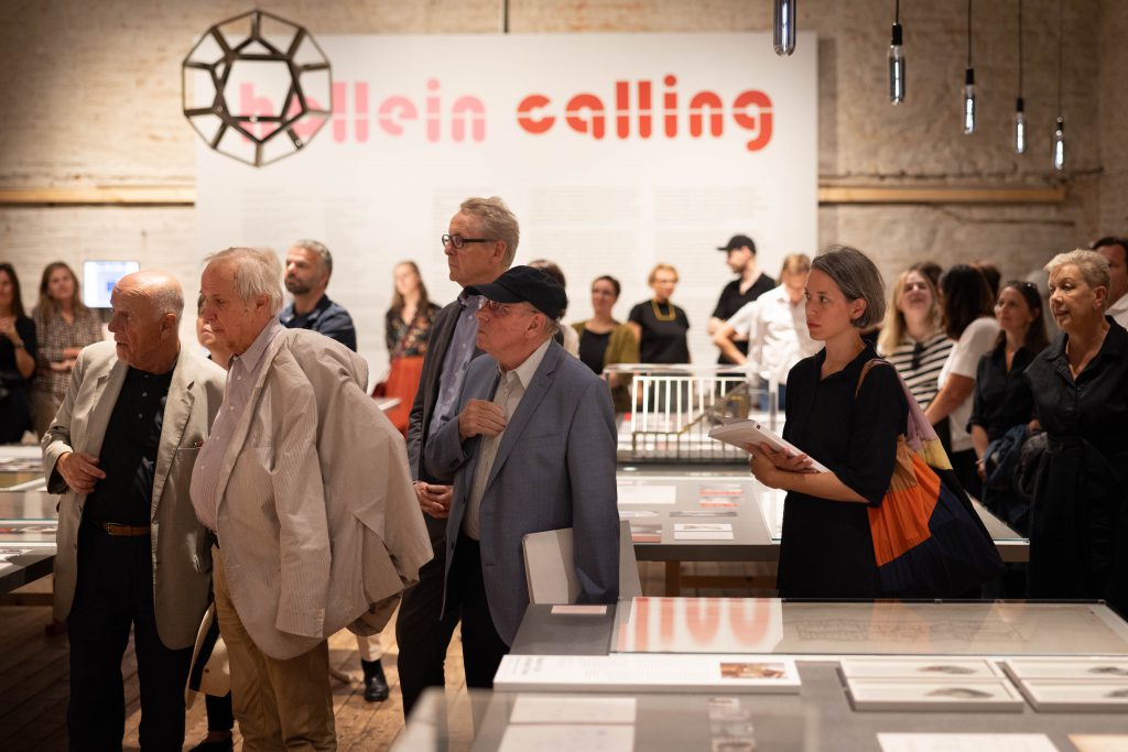 many people in an exhibition room with a large inscribed wall with red letters