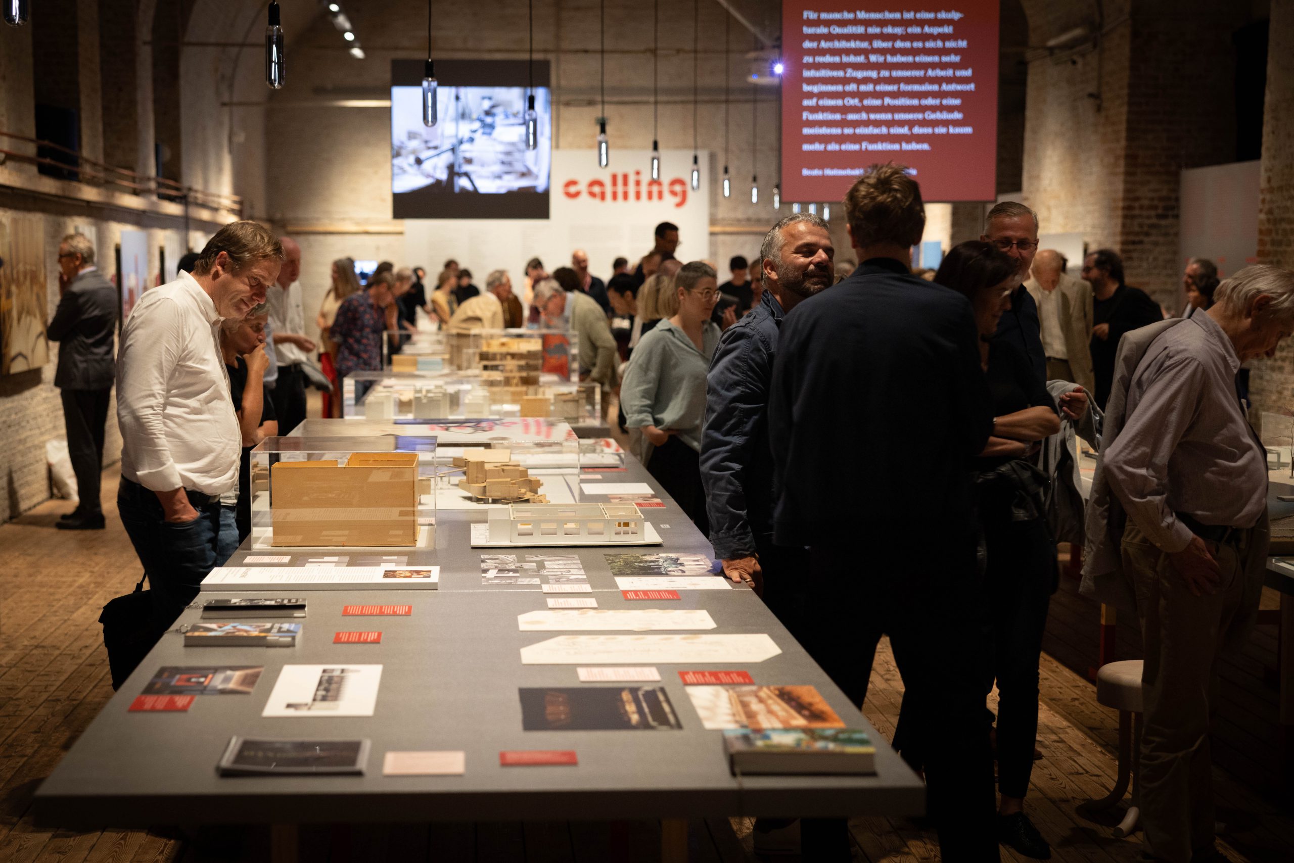 many people in an exhibition with large tables on which there are photos, books models