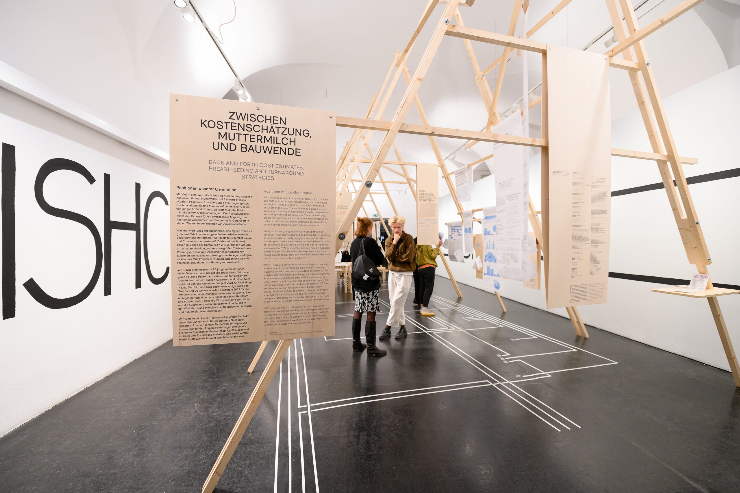 Exhibition room with large panel, behind it 3 people