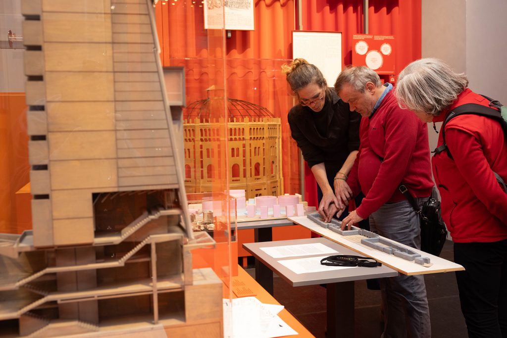 3 people stand in front of an architectural model and touch it