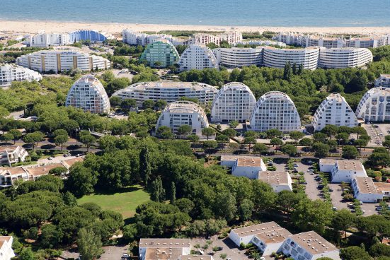 many buildings close to the coast, behind them you can see the beach, the buildings often have a round shape