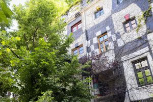 Haus mit bunt gestalteter Fassade und vielen Bäumen drum herum und am Dach